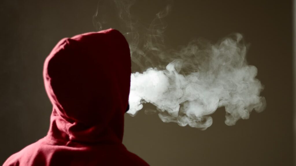 A photo from behind someone who is vaping and exhaling a cloud.